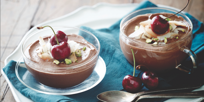 Two dishes of chocolate mousse topped with cherries and pistachio